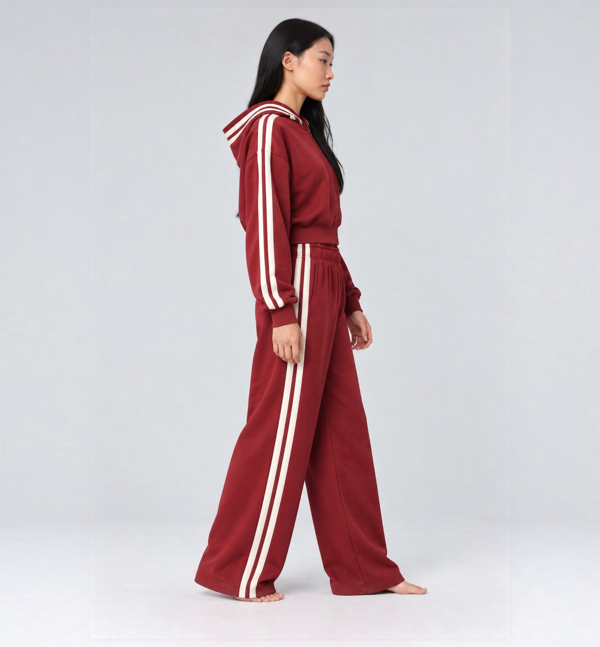 The Weekender Pants in Burgundy by Gallenn – model side view with wide legs and cream side stripes, worn with the matching hoodie